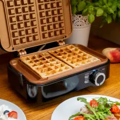 Idealne keto gofry z mascarpone właśnie wyszły z gofrownicy. Na blacie leżą brzoskwinie, a w tle zielona bazylia.