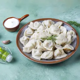 Talerz pełen pysznych, domowych pierogów, obok czosnek, koperek i buteleczka oliwy. Różne rodzaje pierogów zachęcają do spróbowania.
