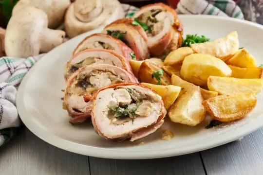 Roladki z piersi kurczaka z pieczarkami, zawinięte w boczek, podane z pieczonymi ziemniakami.