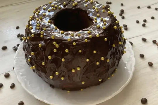 Szybka babka z majonezem i kakao, oblana błyszczącą czekoladą i ozdobiona złotymi kuleczkami.