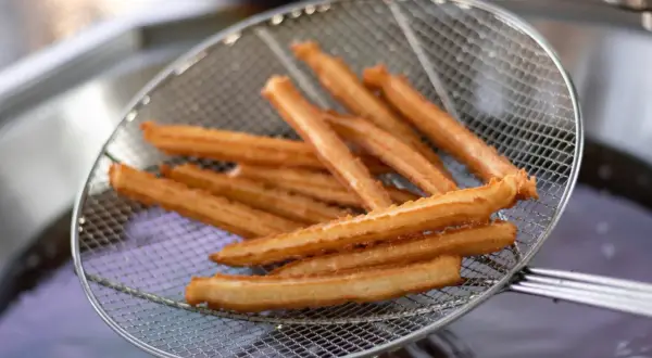 Churros co to? Złociste, chrupiące paluszki smażone na głębokim oleju, wyciągane właśnie na sicie.
