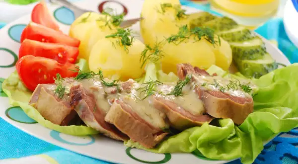 Kawałki ozorków w sosie chrzanowym, podane z ziemniakami, pomidorami i ogórkiem kiszonym. Danie ozdobione jest świeżym koperkiem.