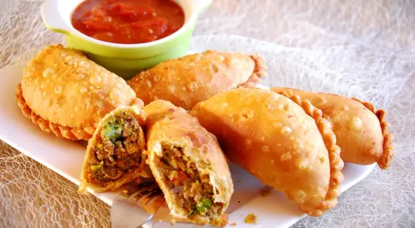 Złociste empanadas, jedna przekrojona, odsłaniająca aromatyczne nadzienie mięsne i warzywne, podane z sosem pomidorowym.