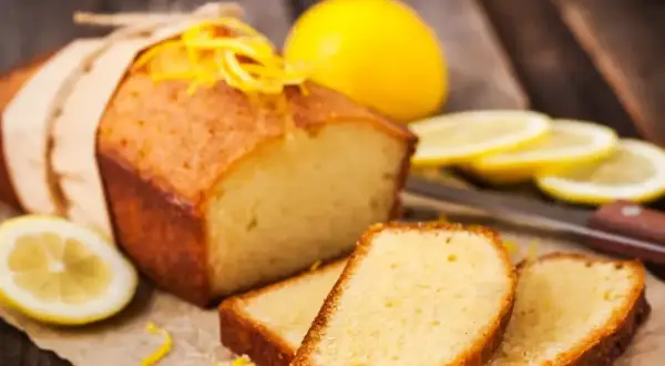 Babka piaskowa przepis babci. Puszysty, cytrynowy keks, ozdobiony skórką cytrynową, z plasterkami cytryny w tle.
