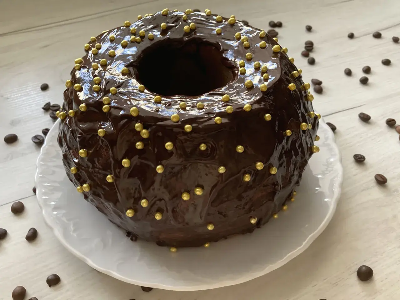 Szybka babka z majonezem i kakao, oblana błyszczącą czekoladą i ozdobiona złotymi kuleczkami.