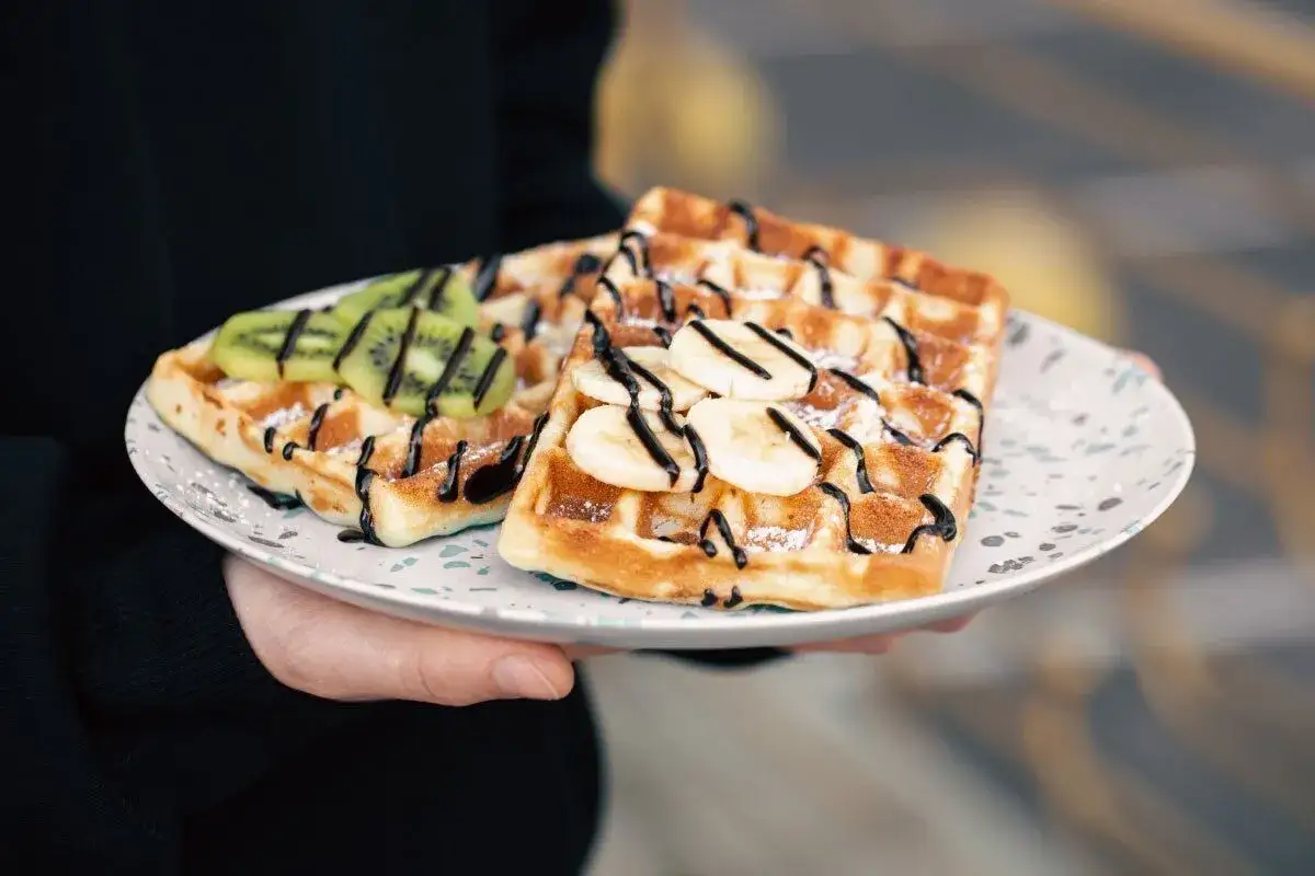 Pyszny gofr belgijski z bananem i kiwi, polany czekoladą, na talerzu.