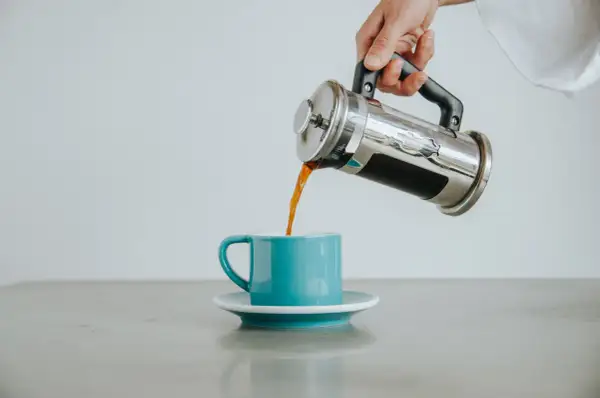 Ręka nalewa aromatyczną, czarną kawę z zaparzacza do turkusowej filiżanki.